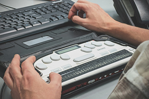 Decorative photo of person using a braille writer with a computer.